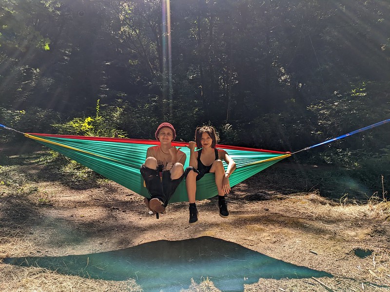 Two teenagers sitting on hammock in sunlit forest